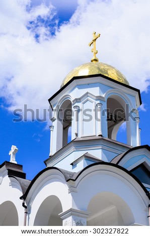 Traditional Christian Orthodox white church with golden domed tower bell and crosses under a cloudy sky