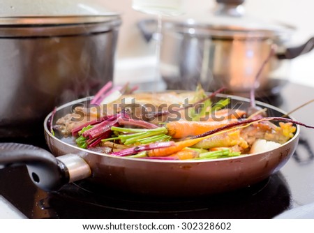 Healthy dinner simmering in a pan with a portion of cooked meat and assorted farm fresh young vegetables, close up view