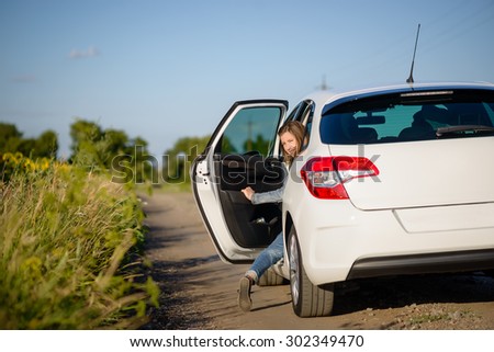 Young woman climbing into the rear passenger seat of a car stopped on a country road looking back to smile at the camera