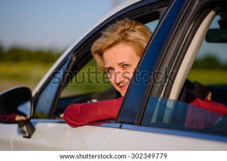 Smiling middle-aged female driver poking her head out of the open side window and turning to smile at the camera
