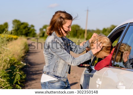 Two women fighting at the roadside on a rural road with one inside and one outside the car fighting through the open drivers window
