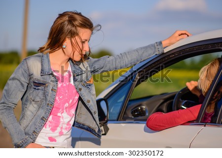Two women chatting at the roadside with a young woman leaning against a car chatting to the female driver, close up view