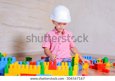 Creative young boy playing with a collection of multicolored building blocks wearing a hardhat as he pretends to be an architect or engineer