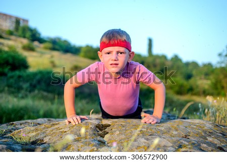 Athletic Young Boy Forcing his Body to Lift While Doing Push Up Exercise on Top of a Big Rock with Sacrificing Facial Expression.