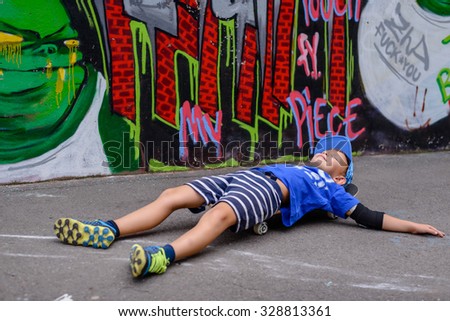 Laughing young boy with his skateboard relaxing in front of a colorful wall covered in graffiti balancing on his back on his board looking up at the sky