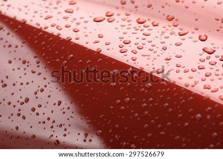 Water drops collect on top of metal red car surface