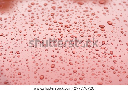 Water drops collect on top of metal red car surface