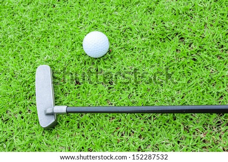 golf ball on a tee and putter in green grass course