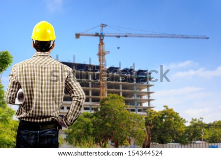 architect with holding blueprints looking at the blurred construction background in blue sky