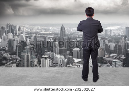 rear view businessman standing cross one\'s arm chest against balcony overlooking city dusky before rain falling