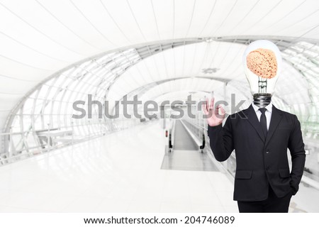 businessman have brain inside a light bulb posed gesturing ok sign while standing at futuristic airport interior with concept of real estate and engineering for success business creativity