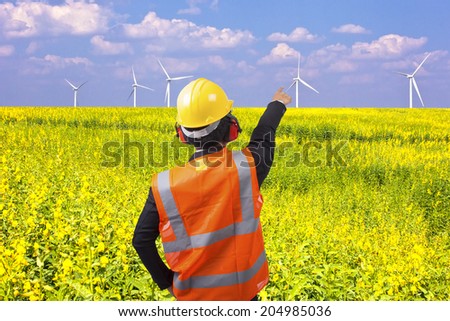 rear view of a engineer in suit pointing at wind turbines in a flower field eco power concept