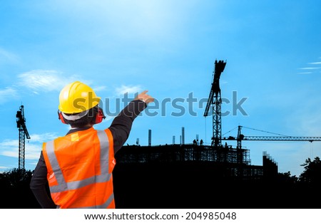 rear view of a engineer in suit pointing at construction site silhouetted on daytime