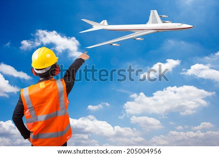 rear view of a air traffic controller in suit pointing airplane at the airport on blue sky background
