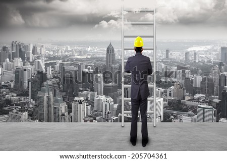 rear view of engineer standing near ladder going up in high sky against balcony overlooking city dusky before rain falling