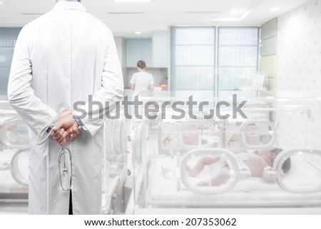 rear view image of doctors with stethoscope in a hospital pose arms crossed behind back looking at newborn in incubator