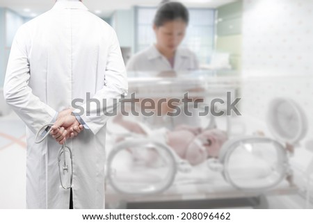 rear view image of doctors with stethoscope in a hospital pose arms crossed behind back looking at newborn in incubator and nurse women care