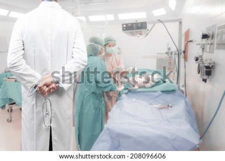 rear view image of doctors with stethoscope in a hospital pose arms crossed behind back looking at baby and team surgeon in operating room