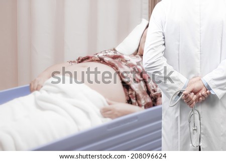 rear view image of doctors with stethoscope in a hospital pose arms crossed behind back looking at  female patient pregnant