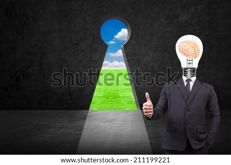 businessman thumb up and head brain inside a light bulb standing front of key hole on old grunge black wall against green grass field and bright blue sky background