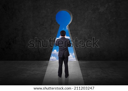 rear view businessman standing cross one's arm front of keyhole on old grunge black wall against blue sky background