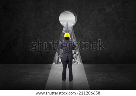 rear view engineer standing cross one's arm and yellow helmet for workers security front of keyhole on old grunge black wall against urban scene balcony over looking city dusky before rain falling