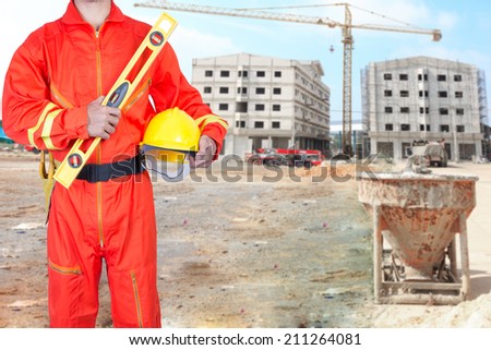technician in uniform holding hard hat and yellow construction spirit level at the front of blurred construction site