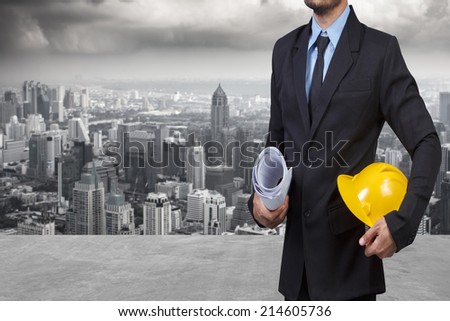 engineer holding helmet and blueprints against urban scene balcony over looking city dusky before rain falling