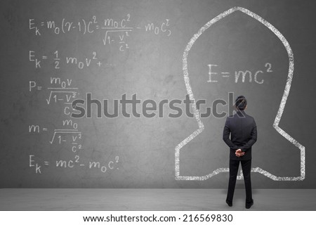 Concept of a businessman that solves problems of Albert Einsteins physical formula on concrete wall background