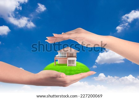 house in human hands representing home ownership and the real estate business against blue sky