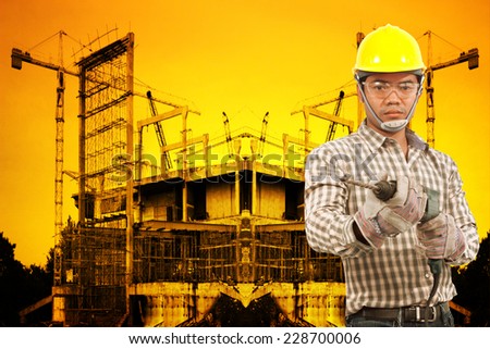 technician in protective safety equipment with drill working at building construction site against beautiful sunset selective focus at eye