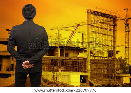 rear view of businessman looking to the future building construction crane with beautiful sunset
