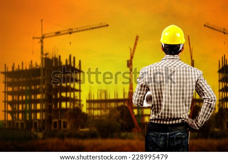 technician builder in protective safety equipment goggles hard hat and blueprints working at high building construction site against beautiful sunset