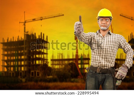 technician builder in protective safety equipment goggles hard hat and thumb up concede working at high building construction site against beautiful sunset