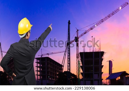 rear view business man pointing to the future against silhouette of crane and building construction and beautiful sunset sky