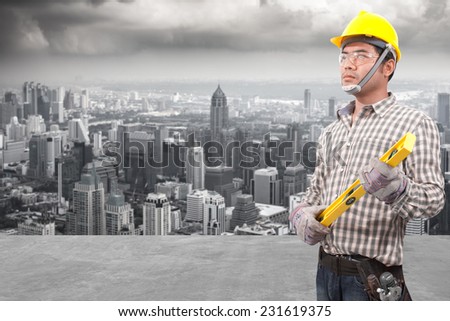 technician builder in protective safety equipment goggles hard hat and water level working at high building construction site against urban scene balcony over looking city dusky before rain falling