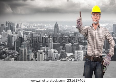 technician in protective safety equipment goggles hard hat and thumb up concede working at high building construction site against urban scene balcony over looking city dusky before rain falling