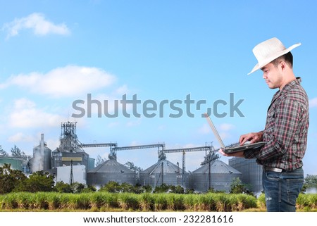 modern farmer checking his field plant and working on laptop computer against corn dryer silos in concept of industrial and agriculture