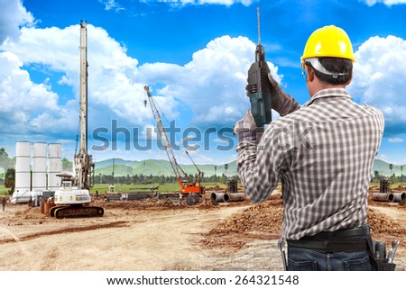 technician in protective safety equipment with drill and tool belt working in building construction site against blue sky