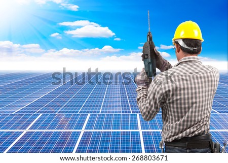 technician in protective safety equipment with drill and tool belt working at solar energy power plant against beautiful sky with in concept ecology