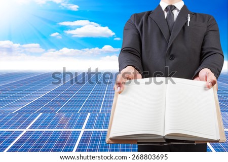 business man holding book blank for workspace at solar energy power plant against beautiful sky with in concept ecology