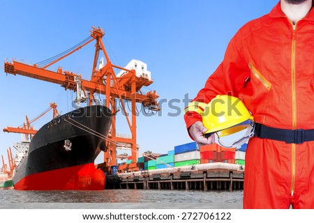 Container ship being unloaded with dock worker holding hard hat controlling work process in the harbor