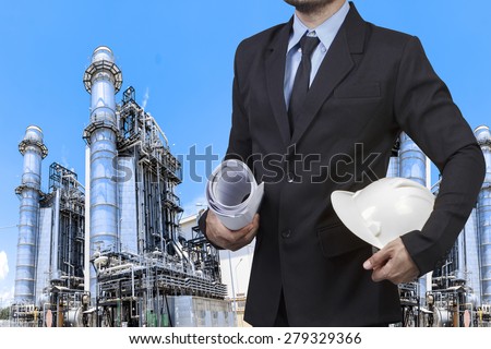 Engineer holding blueprint and hard hat at equipments and machinery with modern thermal power plant in refinery