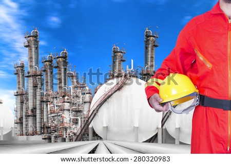 Engineer holding hard hat for working at pipe line connection to oil tanks in petrochemical oil refinery against blue sky