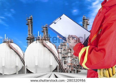 Engineer record clipboard for working at pipe line connection to oil tanks in petrochemical oil refinery against blue sky
