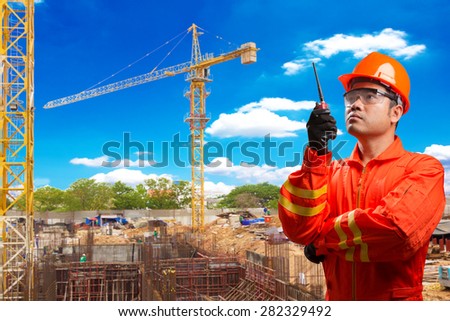 Engineer with radio communication in action for working at footing of building construction site with tower crane and blue sky