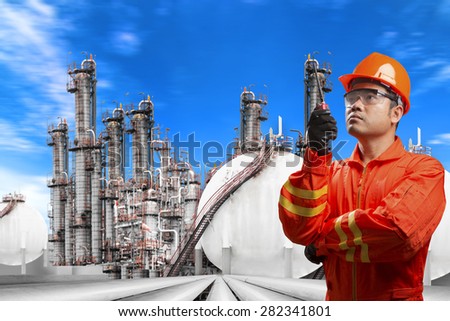 Engineer with radio communication in action for working at pipe line connection to oil tanks in petrochemical oil refinery against blue sky