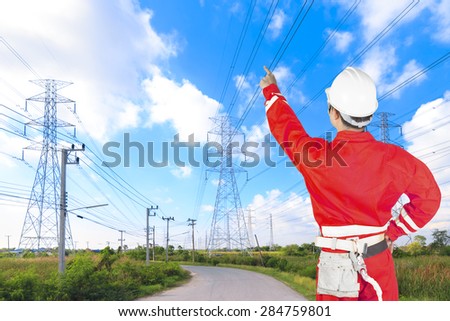 Engineer pointing at high voltage power pylon against blue sky