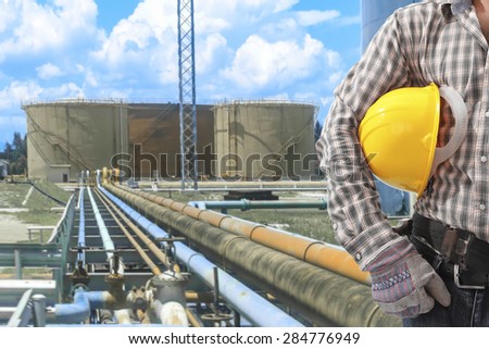 Worker holding hardhat for working at pipe line connection to oil tanks in petrochemical oil refinery
