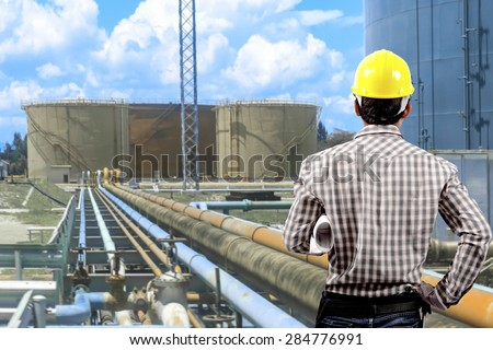 Technician holding blueprint for working at pipe line connection to oil tanks in petrochemical oil refinery